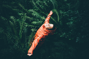 The young woman with orange raicoat smiles and laughs under the rain. Girl enjoying warm summer rain at the tropical forest. Сoncept of nature and happy life, adventure.