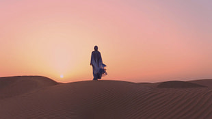 Portrait of beautiful Arab woman weared in blue traditional dress in the desert during sunset.
